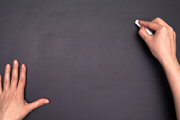 Close-up of hands writing with a chalk on an empty blackboard. Many copy space for text.