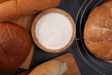 Freshly baked bread loaf bun roll round long mix verity flour in wooden bowl on wooden board metal grill over black background