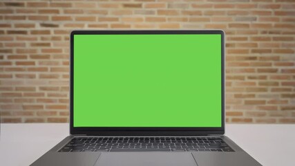 Close up display computer desktop with mock-up green screen on white table, Slow motion laptop green screen on desk and brown brick wall background, Blank of mockup notebook PC, Chroma key monitor.