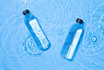 Wall Mural - Water bottle in clean transparent water with sunlight on blue background,top view