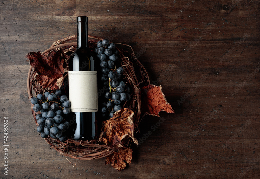 Bottle of red wine with grapes and dried vine leaves on an old wooden background. - obrazy, fototapety, plakaty 