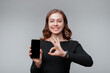 © AstiMak - Portrait of a nice young brunette woman holding smartphone and showing OK sign, girl recommend upload new app