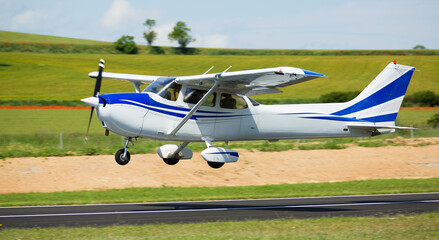 View of sports airplane in motion over runway on background with picturesque landscape.