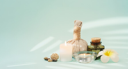 Concise spa composition with candles, flower, oil flask, herbal ball, and other decor elements on turquoise background.