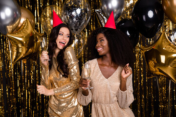 Sticker - Photo of two optimistic brunette curly hairdo ladies with balloons glass wear hat nice dress isolated on gold background