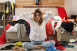 © New Africa - Young woman surrounded by different clothes in messy room. Fast fashion concept