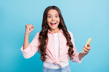 Canvas Print - Photo of young excited crazy positive girl raise fist in victory with open mouth hold phone isolated on blue color background