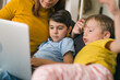 © cherryandbees - mother using laptop computer with her sons. they are sitting on sofa at home