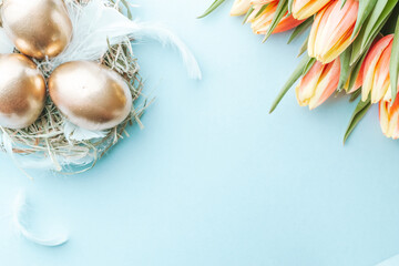 Wall Mural - Golden eggs in basket with spring tulips, white feathers on pastel blue background in Happy Easter decoration. Foil minimalist egg design, modern top view design.