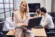 © Roman - Confident young woman in formal clothes, working on laptop and looking on the camera sitting at his workplace in the office
