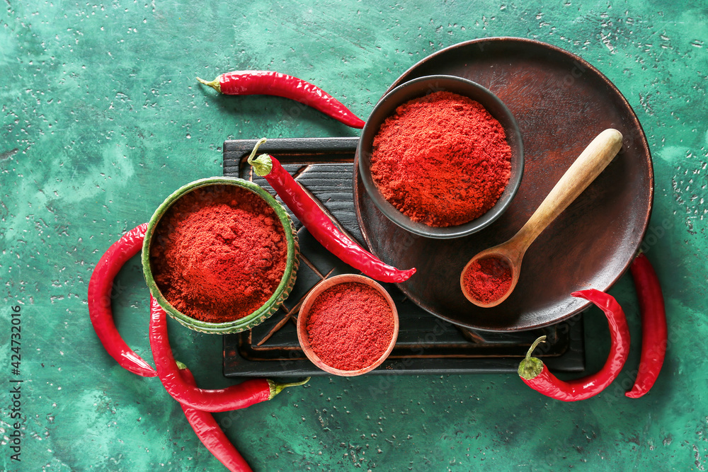 Bowls and spoon with red chili powder on color background
