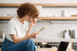 © Drobot Dean - Young curly woman reading her notes while sitting on table at kitchen