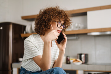 Wall Mural - European curly woman talking on cellphone while sitting on table