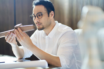 Asian bearded designer sitting, thinking and sketching ideas indoors