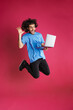 Excited brunette man gesturing and using laptop while jumping