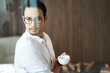 © allensima - confident Asian businessman standing behind glass drinking coffee looking down at the city