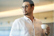 © allensima - confident Asian businessman standing behind glass drinking coffee looking down at the city