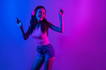 Poster - Photo of young smiling excited funky woman look copyspace dancing in headphones isolated on neon blue color background