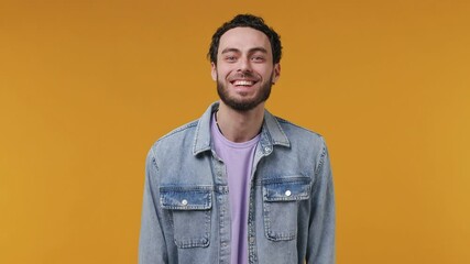 Wall Mural - Calm unshaven bearded young man 20s in denim jacket purple t-shirt looking camera surprised ask what doing winner gesture say yes celebrating isolated on yellow color wall background studio portrait