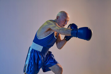 Senior man wearing sportwear boxing isolated on gradient studio background in neon light. Concept of sport, activity, movement, wellbeing. Copyspace, ad.