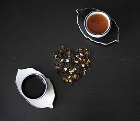 Beautiful black and white tea ceremony set: small cups and saucers in the form of leaves next to a scattering of tea with pieces of dried citrus and sugar snowflakes on the background of a black woode