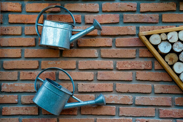 Two watering can hanging on brick wall in back yard garden at home.Gardening concept.