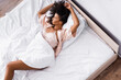 © LIGHTFIELD STUDIOS - Top view of curly african american woman lying near smartphone on bed