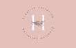 © ankreative - White Letter H Logo with circle lettering design and outline leaves and pastel backgound.