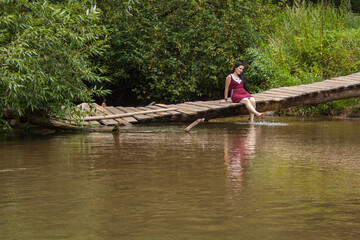  Girl sitting on a wooden bridge over the river and reading a book