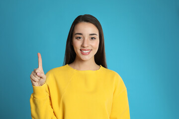 Wall Mural - Woman showing number one with her hand on light blue background