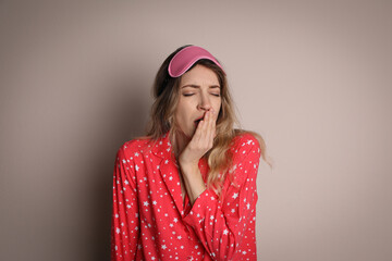 Poster - Young tired woman with sleeping mask yawning on beige background