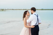 © omelnickiy - young couple a guy in black breeches and a girl in a pink dress are walking along the white sand