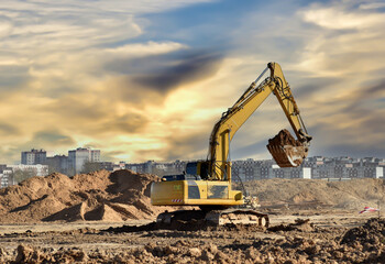 Excavator during earthmoving work at construction site on sunset background. Backhoe digging ground for foundation pit. Open pit development. Construction of new houses and buildings in the city.