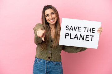 Wall Mural - Young caucasian woman isolated on pink background holding a placard with text Save the Planet and pointing to the front