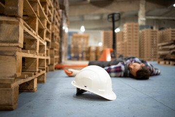 Injury at work. Warehouse worker lying unconscious on the concrete floor after the fall. Focus on hardhat.