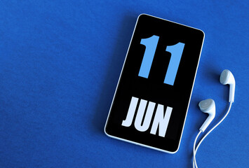 June 11. 11 st day of the month, calendar date. Smartphone and white headphones on a blue background. Place for your text. Springtime month, day of the year concept