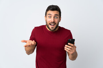 Poster - Young handsome man with beard using mobile phone isolated on white background with shocked facial expression