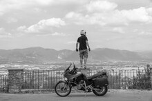 A Lightly Dressed Man And His Adventure Motorcycle. No Protection, Only Helmet. Sunny Day In Narni, Italy. Green Mountains In The Background. Vacation And Travel Concept. Distance Look.