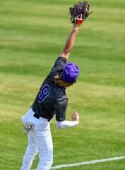 Action photo of athletic high school baseball player making an amazing play during a baseball game