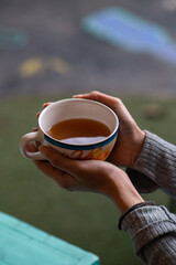 Manos agarrando taza de té de flores con fondo desenfocado