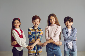 Portrait of a smiling group of children standing against the gray wall and holding hands. Concept of socialization, interaction, cooperation and relationships with peers.