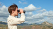 © Érik Glez. - A side view of a young traveler from Spain in a white shirt looking over mountains through binoculars