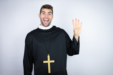 Young hispanic man wearing priest uniform standing over white background showing and pointing up with fingers number four while smiling confident and happy