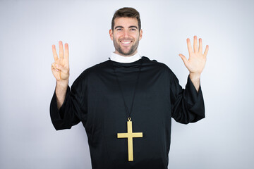 Wall Mural - Young hispanic man wearing priest uniform standing over white background showing and pointing up with fingers number eight while smiling confident and happy