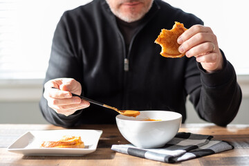 Middle age man eating a steaming bowl of tomato soup and a sandwich