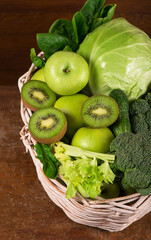 Wall Mural - Green vegetables - kiwi, cabbage, herbs, celery, broccoli, cucumbers in a basket a wooden background