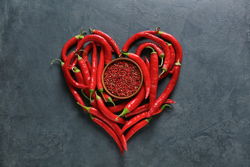 Heart made of chili peppers and bowl with red peppercorns on dark background