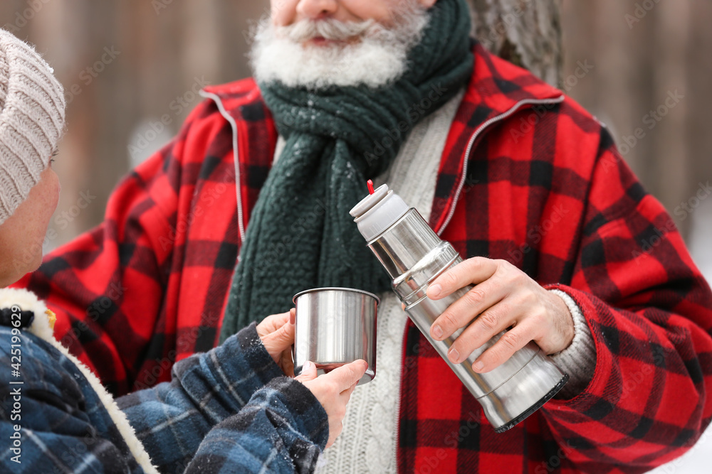 Happy mature couple drinking hot tea in forest on winter day