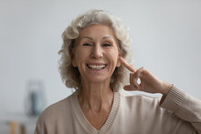 Portrait Of Happy Senior Woman Pointing Finger At Her Ear, Looking At Camera And Smiling. Excited Mature 60s Lady Enjoying Hearing Ability After Deafness Therapy. Deaf Patient Communication. Head Shot