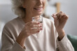 © fizkes - Smiling elderly female patient holding pill and glass of water. Senior mature woman taking daily dose of prescribed meds against depression, mental disorders, flu, insomnia, pain. Elderly treatment